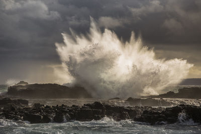 Sea waves splashing on rocks against sky