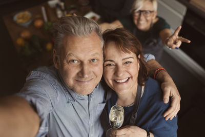 Cheerful mature man with arm around woman while taking selfie in kitchen