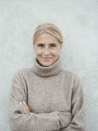 Smiling woman with arms crossed in front of wall