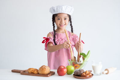 Portrait of smiling girl preparing salad against white background