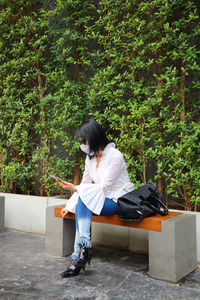 Woman sitting on seat against plants