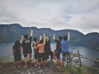 Friends pointing against mountains by lake against cloudy sky