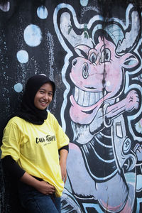 Portrait of smiling young woman standing against graffiti