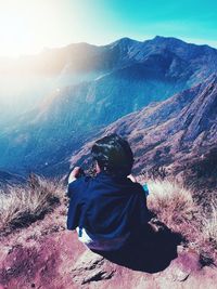 Rear view of man sitting on mountain against sky