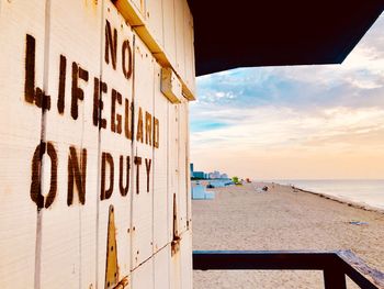 Text on lifeguard hut at beach against sky during sunset