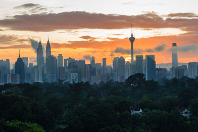 Trees and buildings against cloudy sky during sunset