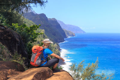 Woman sitting on rock by sea against sky