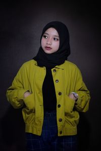 Portrait of young woman standing against black background