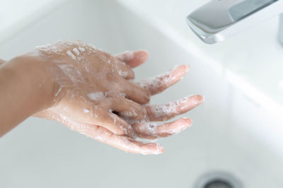 Cropped image of hand touching water from faucet at home