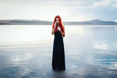 Young woman standing in lake against sky