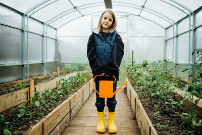 A girl stands in a greenhouse with a watering can, caring for a crop on a farm