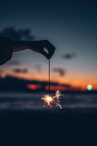 Cropped hand of woman holding illuminated sparklers during sunset