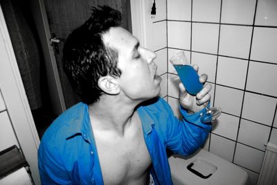 Portrait of shirtless man drinking water in bathroom