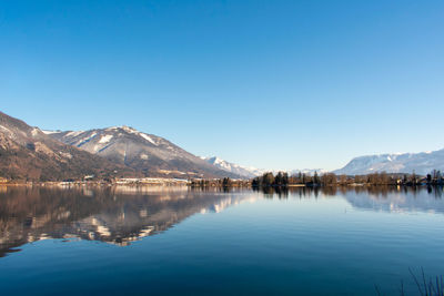 Scenic view of lake by mountains against clear blue sky