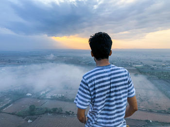 Rear view of young man looking at cityscape against sky