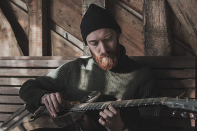 Young man playing guitar while sitting against wall