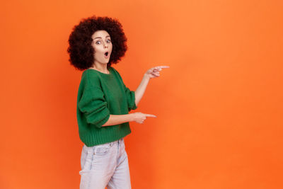 Portrait of young woman with arms raised standing against yellow background