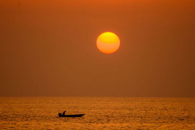 Silhouette boat in sea against orange sky