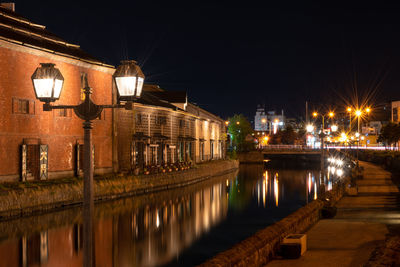 Illuminated street by river and buildings at night