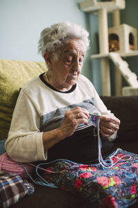 Portrait of crocheting senior woman sitting on couch at home