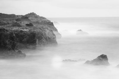Scenic view of long exposure photo of rocks in sea against sky