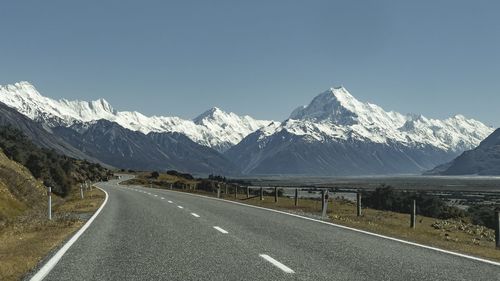 Road by snowcapped mountains against clear blue sky
