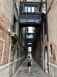 Rear view of woman walking on alley amidst buildings in city