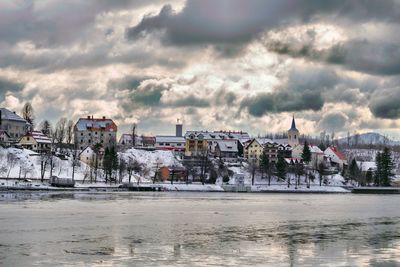 Buildings by river against sky in city during winter