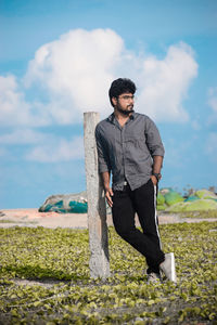 Portrait of young man standing at beach against sky