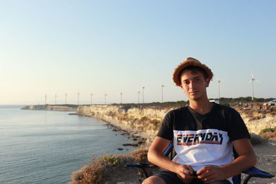 Portrait of young man sitting against clear sky