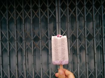 Hand holding ice cream cone against chainlink fence