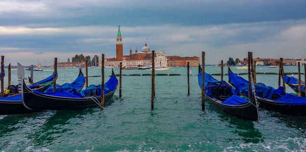Boats moored in canal by buildings against sky