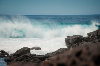 Waves splashing on rocks at shore against sky