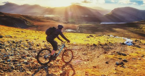 Side view of person riding bicycle on hill during sunny day