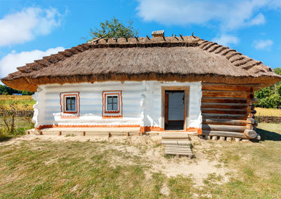 Vintage traditional ukrainian rural house with a thatched roof and wicker fence against a blue sky.