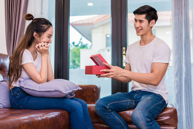 Boyfriend giving gift to girlfriend while sitting on sofa at home