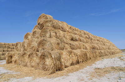 Hay bales on field against blue sky