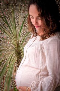 Side view of pregnant woman standing by plant