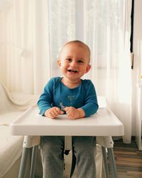 Cheerful baby sitting on high chair at home
