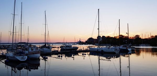 Sailboats moored in harbor at sunset