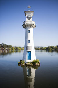 Lighthouse by lake against clear blue sky