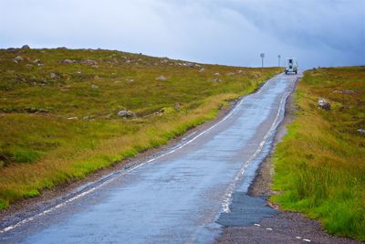 Country road amidst field against sky