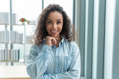 Portrait of young woman standing against window