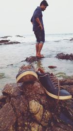 Full length of man standing on rock at beach against sky