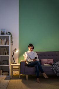 Woman using smart phone while sitting on sofa at home