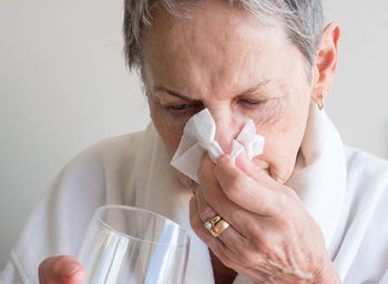 Close-up of woman cleaning nose with facial tissue against wall