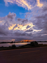 Scenic view of road amidst field against sky at sunset