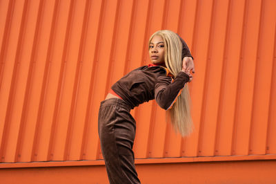 Cheerful african american woman in sportswear dancing in the street on an orange background