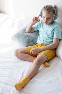 Cute boy listening to music in earphones seating on bed. child wearing headphones listens to music.