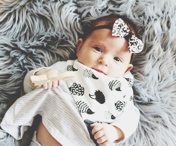 Portrait of cute baby lying on bed at home. monochrome colours, bow, hedgehogs bib, wooden teether.